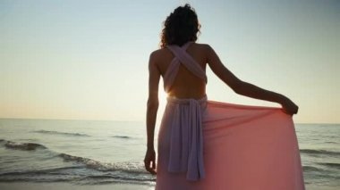 Kadın tutar ve gün batımına karşı elbisesini bırakır.