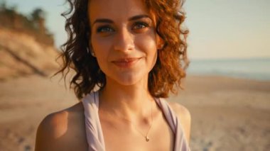 Pretty woman with smiling face is looking at you against sunset sea background