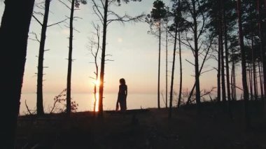 Pretty woman in a long dress is walking against sunset sea background