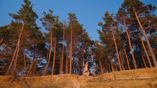 Fit mujer en un vestido largo se está ejecutando contra la puesta del sol bosque y el fondo del cielo — Vídeos de Stock
