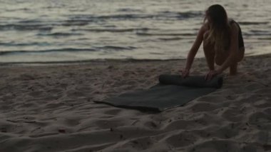Young woman finished training and packs her mat at lake