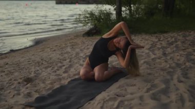 Beautiful and calm woman practices yoga on a sandy beach using a mat in the evening