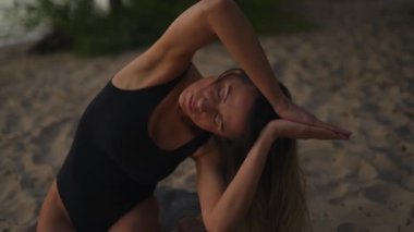 Beautiful and calm woman practices yoga on a sandy beach using a mat in the evening
