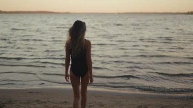 Silhouette: Fit and slim woman walks towards a windy lake and starts practicing yoga in the evening real time