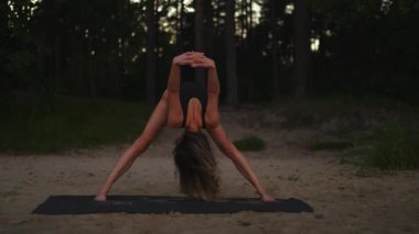 Young woman practices yoga on a sandy beach using a mat in the evening