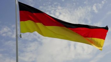 Large German flag waving on a pole against blue sky slow motion