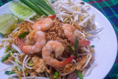 Tahta masadaki beyaz tabakta taze karidesli Pad Thai.