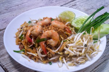 Tahta masadaki beyaz tabakta taze karidesli Pad Thai.