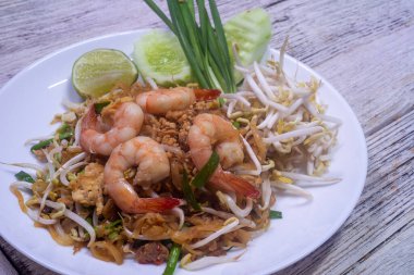 Tahta masadaki beyaz tabakta taze karidesli Pad Thai.