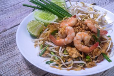 Tahta masadaki beyaz tabakta taze karidesli Pad Thai.