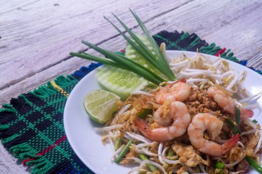 Tahta masadaki beyaz tabakta taze karidesli Pad Thai.