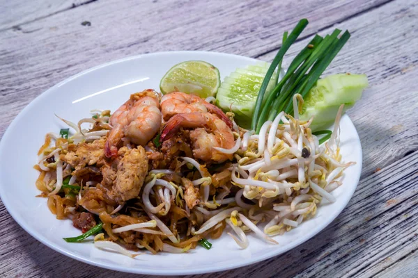 Tahta masadaki beyaz tabakta taze karidesli Pad Thai.