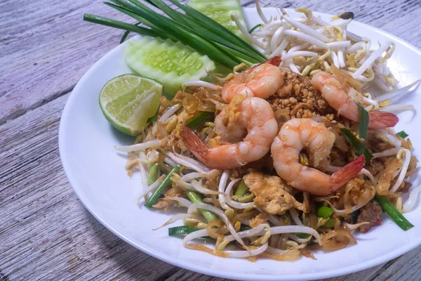 Tahta masadaki beyaz tabakta taze karidesli Pad Thai.