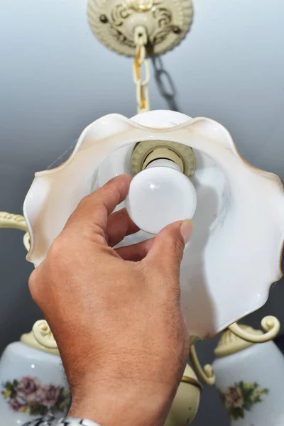 man changing a light bulb to the chandelier attached to the ceiling of a room