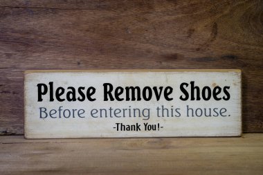 Close up wooden sign please remove shoes sign with the message Please Remove Shoes Before Entering This House.
