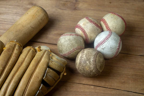 Close up old baseball, wooden baseball bat and baseball glove on a woodeb table. select focus.