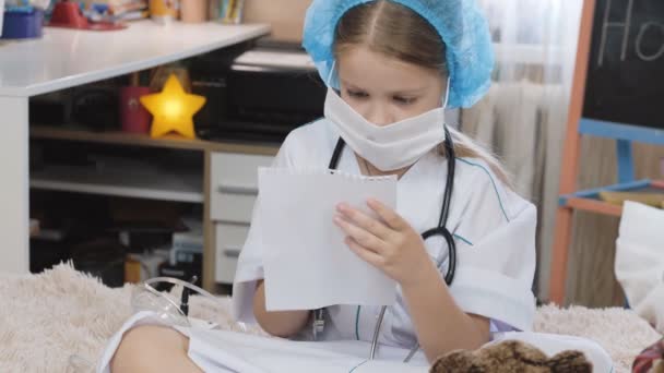 Playing at the Hospital at home. Doctor writing in a notebook. little girl doctor role playing. — Video Stock