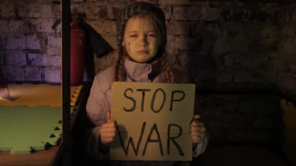 Miúda ucraniana protestando conflito de guerra levanta bandeira com inscrição, Mensagem, texto Stop War sentado no abrigo, porão. Crise, paz, agressão, criança contra a guerra. — Vídeo de Stock