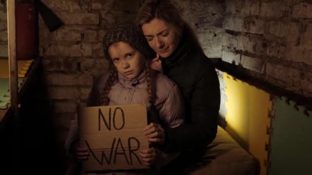 ウクライナの母親と娘、女の子、子供の戦争の紛争に抗議碑文、メッセージ、テキストは戦争の避難所、地下に座ってバナーを発生させます。危機、平和、侵略、戦争に対する子供. — ストック動画