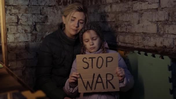 Mãe e filha ucraniana, menina, criança protestando conflito de guerra levanta bandeira com inscrição, mensagem, texto Stop War. Sentado no abrigo, na cave. Crise, agressão, criança contra a guerra. — Vídeo de Stock
