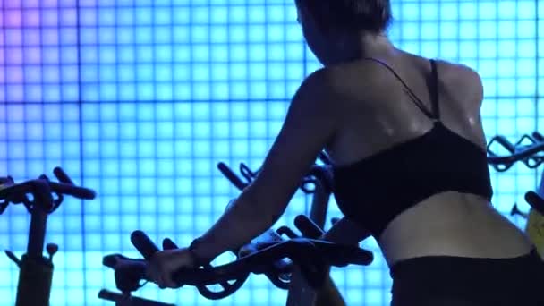 Ajustar a las mujeres. Entrenamiento en una bicicleta estacionaria. Deportes de grupo. Equipo de entrenamiento deportivo en un gimnasio de fitness. Rutina cardiovascular en simuladores. — Vídeos de Stock