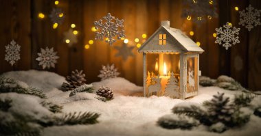 Fenerli ve asılı süslemeli Noel sahnesi, ahşap arka plan ve kar, yanan mum ve kahverengi kalaslar sıcak bir ortam yaratır.