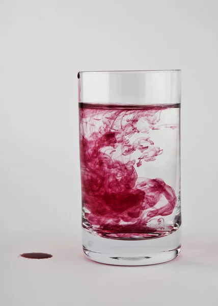 La pintura roja se disuelve en un vaso de agua clara . — Foto de Stock