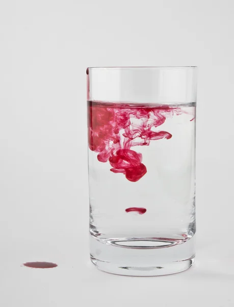 La pintura roja se disuelve en un vaso de agua clara . — Foto de Stock