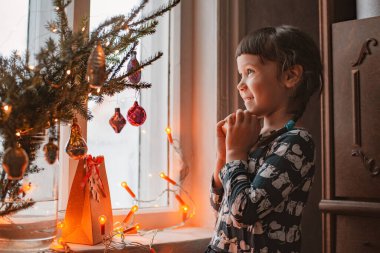 Noel 'de pencerede elinde bir hediyeyle gülümseyen mutlu bir kız bebek. Yeni yıl için bir dilek tut..