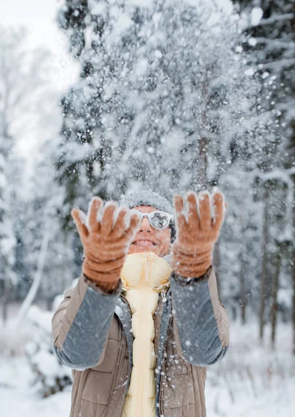 雪の降る冬の日に外を歩く幸せな女性 女性モデルはあなたの手で雪をキャッチし 楽しい雪を吹いて ファッショナブルなグレーのサングラスを身に着けている — ストック写真