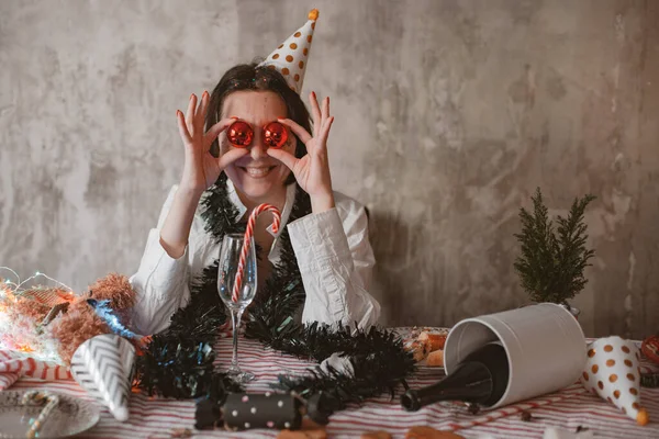 Şenlikli parti şapkalı neşeli genç kadın komik bir şekilde gözlerini Noel baloncuklarıyla kaplıyor. — Stok fotoğraf