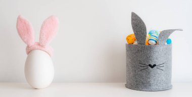 Paskalya minimalist dekorasyonu. Gri keçeli sepet şeklinde bir sürü parlak renkli yumurta kulakları beyaz olan büyük seramik yumurta. Parlak Paskalya tatili, boş yer