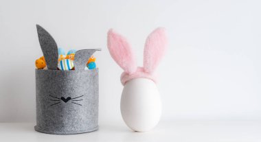 Paskalya minimalist dekorasyonu. Gri keçeli sepet şeklinde bir sürü parlak renkli yumurta kulakları beyaz olan büyük seramik yumurta. Parlak Paskalya tatili, boş yer