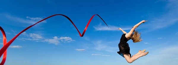 Гімнастка з червоною стрічкою, що стрибає на блакитне небо Стокова Картинка