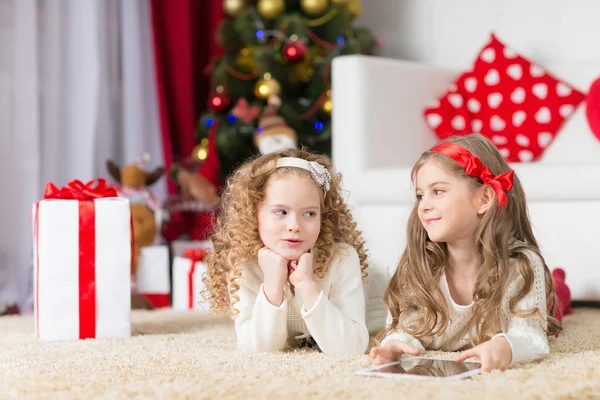 Karácsony, x-mas, tél, boldogság koncepció - két imádnivaló göndör lány játszik tabletta pc — Stock Fotó