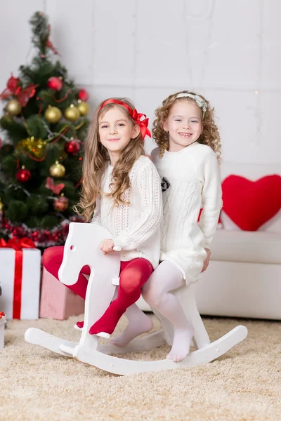 Jul, x-mas, vinter, lycka koncept - två bedårande glada tjejer spelar på häst nära granen — Stockfoto