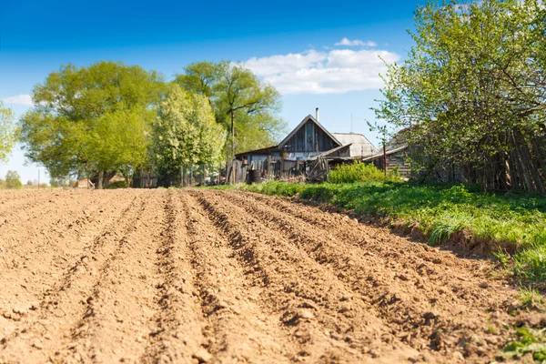 Plowed field on a background of rural houses — Stock Photo, Image