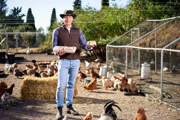 Stolzer junger Mann mit einem Korb voller Eier mit Hühnern hinter sich. — Stockfoto