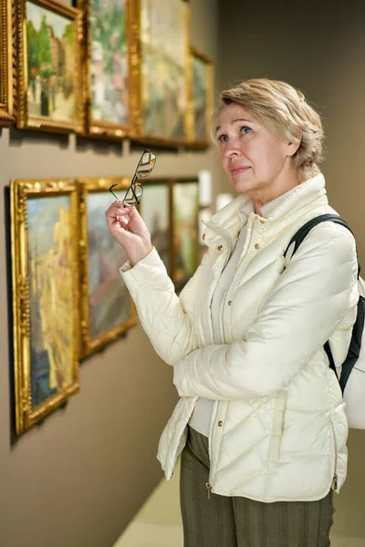 Pensioner woman watching at art collection exhibition in museum — Stock Photo, Image