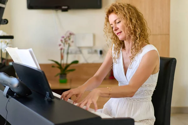Woman in white dress sitting at the piano. Woman playing piano were digitally modified. Practice at home.