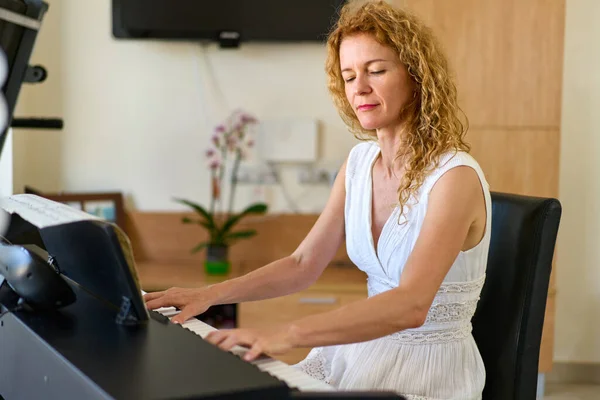 Woman in white dress sitting at the piano. Woman playing piano were digitally modified. Practice at home.
