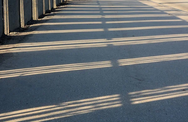 在一个阳光灿烂的冬日 篱笆的阴影笼罩着道路 奇形怪状 — 图库照片