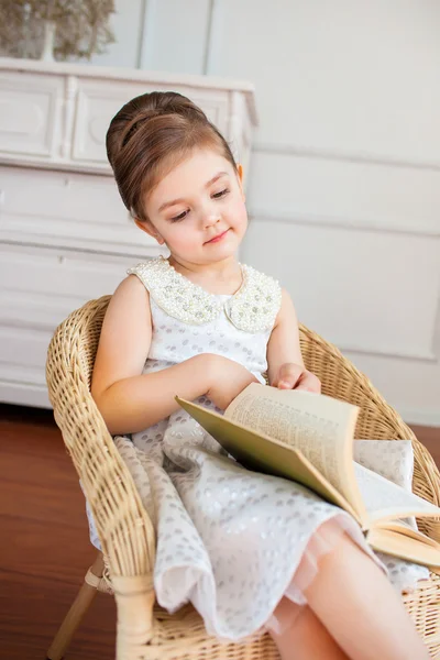 De lachende meisje het lezen van een boek op de leunstoel Stockafbeelding