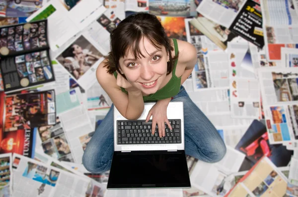 Ragazza con un computer portatile seduto sui giornali — Foto Stock