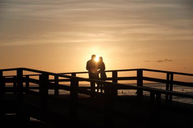 Bir çift âşığın silueti iskelede Sabah doğan güneşin arka planında.
