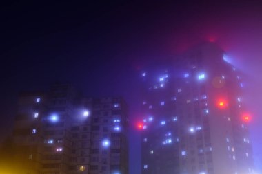 Sisli bir gecede konut binasının pencerelerinden gelen ışık.