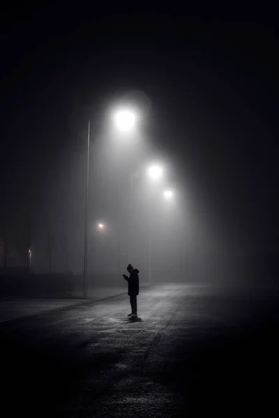 Lonely man under a lamppost at night in the fog on the street.