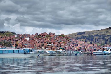 Tourist boats on Lake Titicaca on the background of brick houses in Puno, Peru. clipart