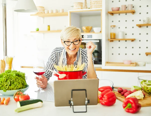 Кухня рецепт приготовления пищи женщина пожилой пенсионный планшет вино бокал технологии созрел счастливым — стоковое фото