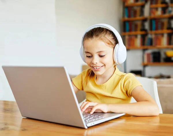 Niño portátil tecnología informática hogar niña educación tarea niño aprendizaje internet infancia estudiante sentado conexión usando auriculares en línea auriculares sonido escuchar Fotos De Stock